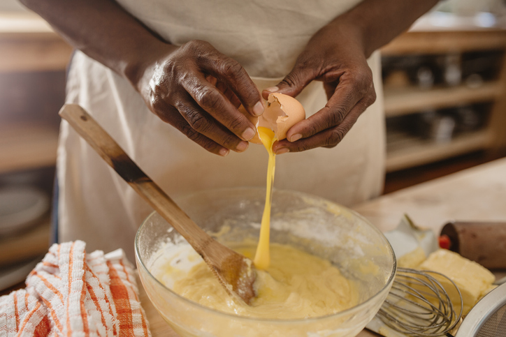 African American woman cracking eggs into a bowl of batter