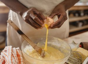 African American woman cracking eggs into a bowl of batter