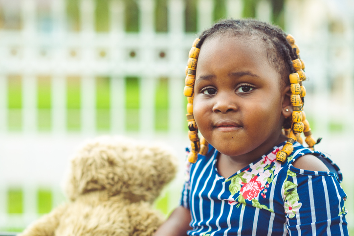 Outdoor portrait of an adorable chubby 3 year old toddler with beads and braids