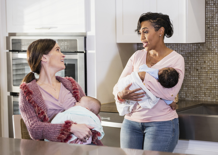 Two mothers nursing babies, conversing in kitchen