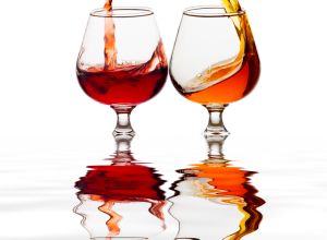 Raising a toast of liquor glasses on a white background reflected on a water surface.