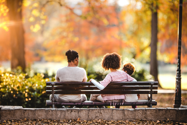 Back view of black family relaxing in autumn day on a park bench.