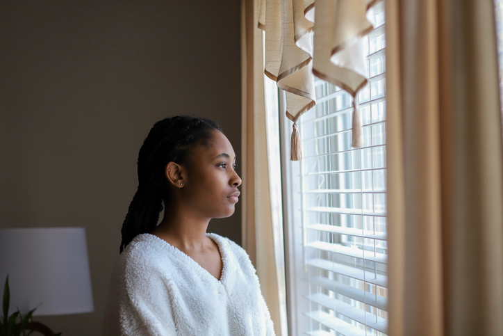 Portrait Of Young Woman Looking Through Window At Home