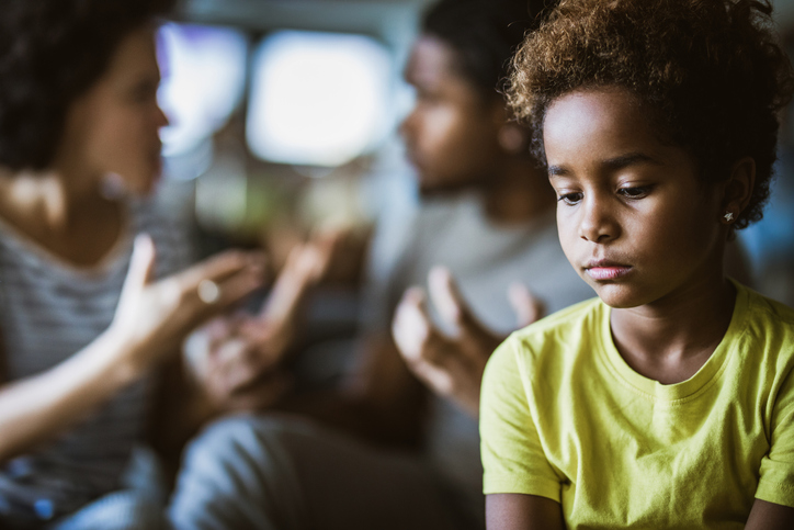 Sad African American girl listening to her parents arguing.