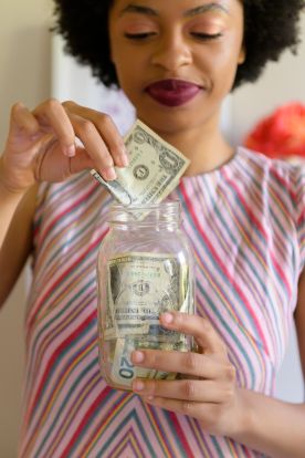 Young woman putting cash into savings jar