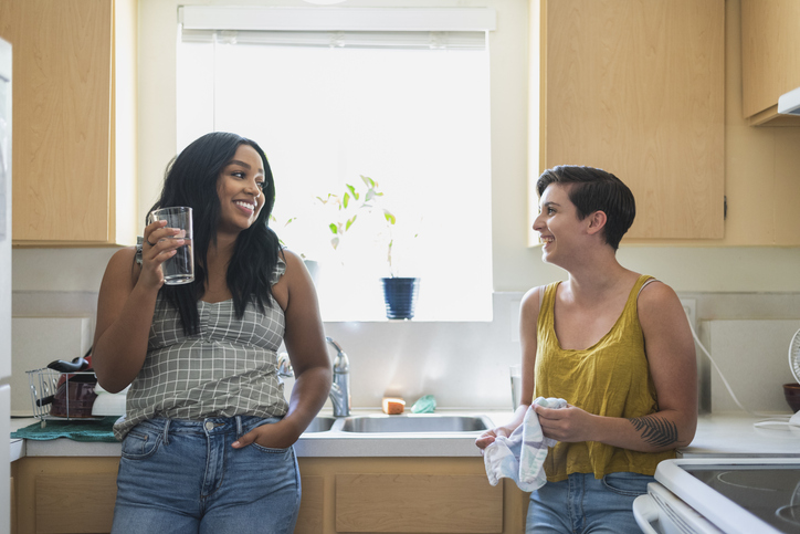 Two young women friends talking together in kitchen