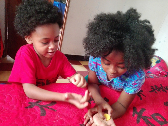 Siblings With Curly Hair Leaning On Bed At Home