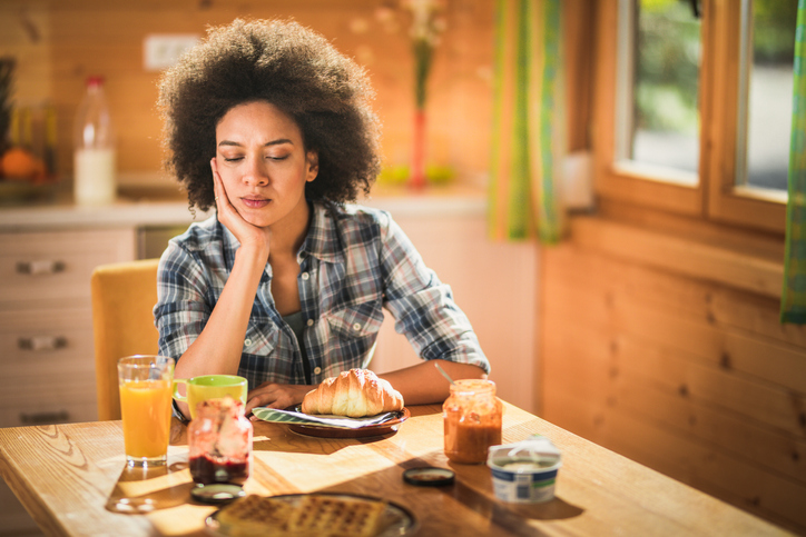 Pensive African American woman sitting at dining table during breakfast time.