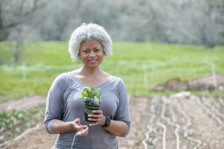 Senior woman smiles while holding plant in garden