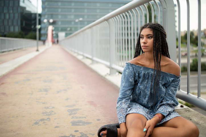 Sad young woman sitting on bridge beside handrail