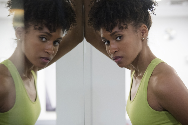 Serious Black woman leaning on mirror wall