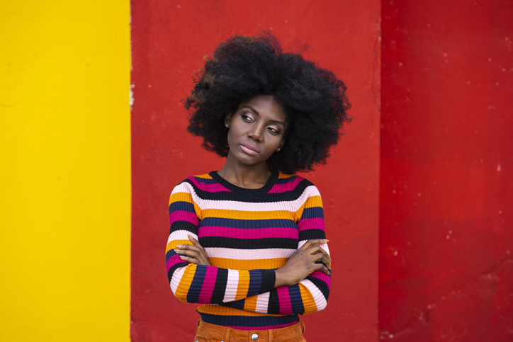 African woman standing arms crossed on red and yellow background