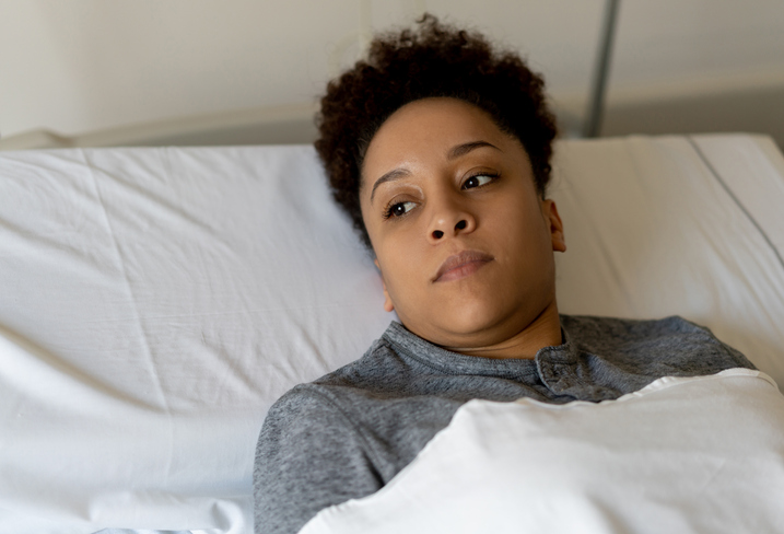 Pensive black young woman looking away while lying down on hospital bed