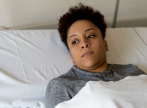 Pensive black young woman looking away while lying down on hospital bed