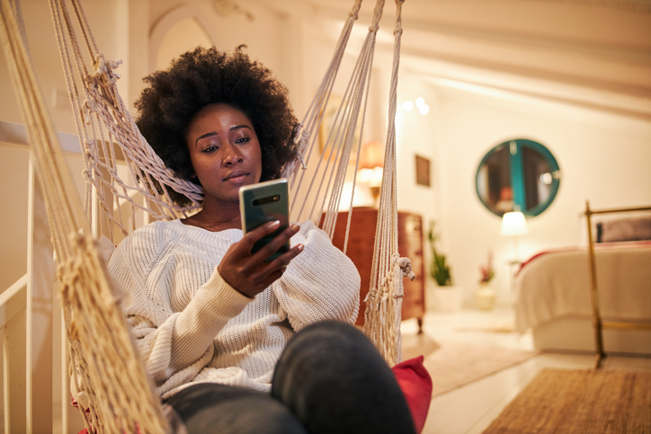 Beautiful black woman using a mobile phone at home in a swing