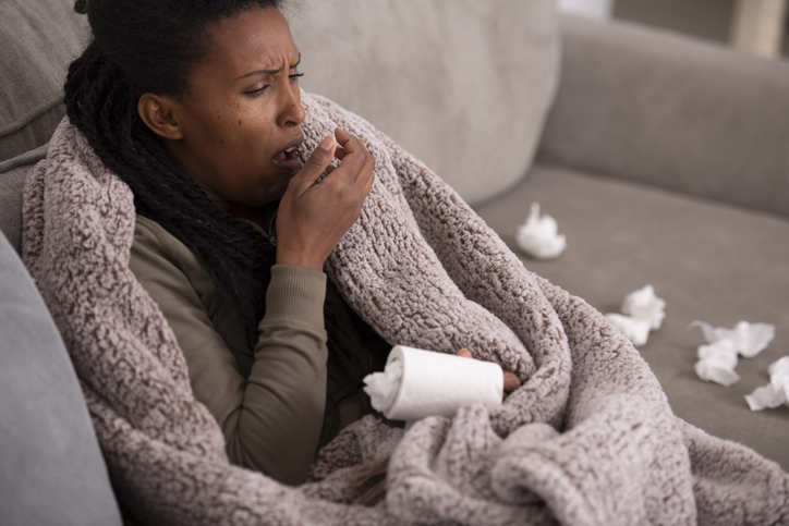 Ill woman coughing covering mouth with the hand, sitting on couch.