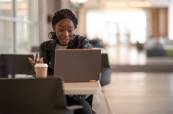 Black woman working at desk on video call, drinking coffee