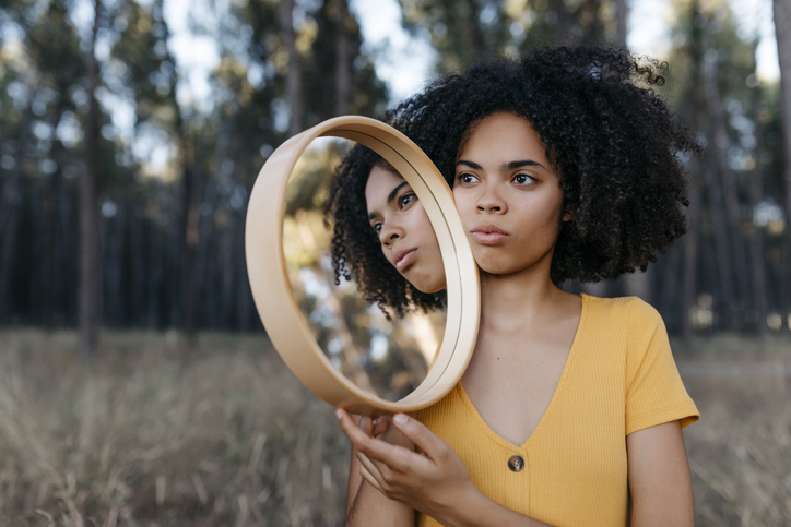 Young woman with afro hair holding mirror in forest