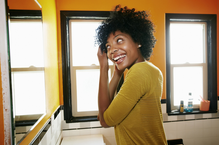 Smiling black woman styling hair in bathroom mirror