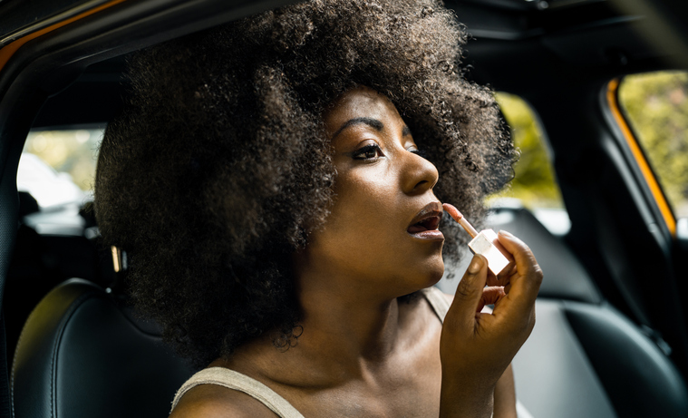 Young black woman adjusting make up in car, mixed race