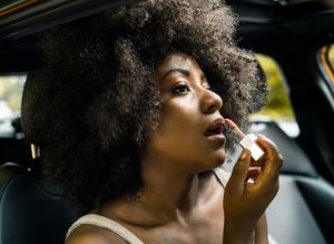 Young black woman adjusting make up in car, mixed race