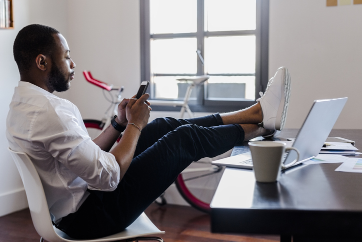 Man using cell phone in home office with feet on desk