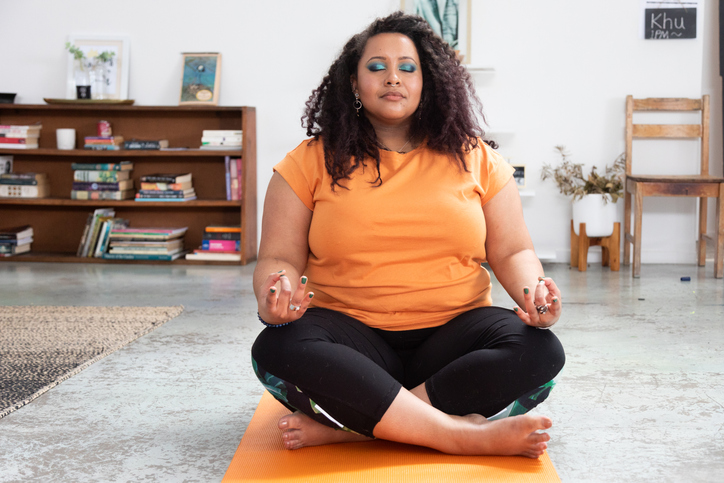 Woman sits in her loft apartment/ studio on yoga mat