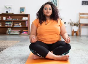Woman sits in her loft apartment/ studio on yoga mat