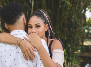 Portrait of young afro couple hugging in a public park. Rear view of the man. Woman looking at camera over the her boyfriend's shoulder.