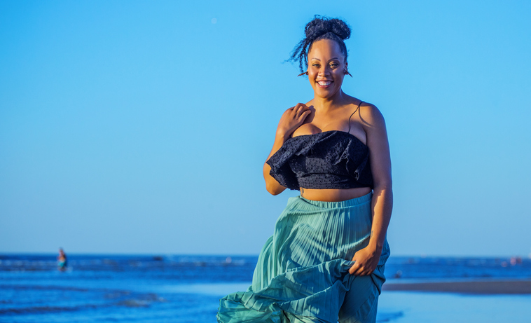 Beautiful Mixed race Woman wearing a long dress on the beach at sunset