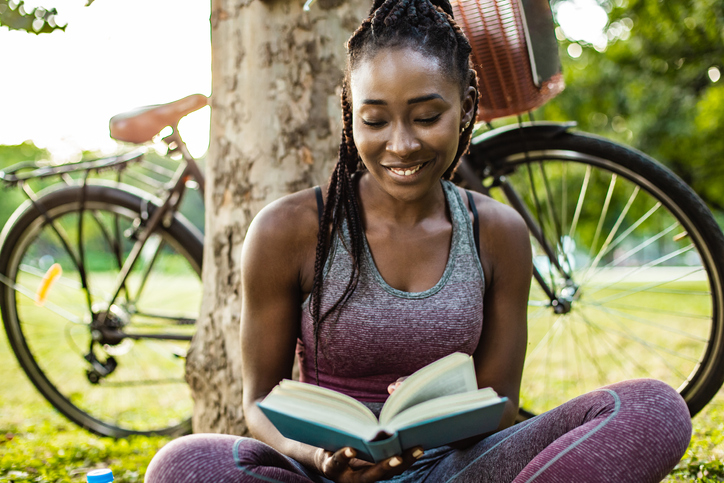 Young African American woman is reading a book in nature