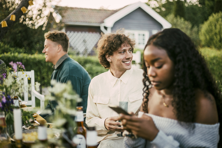 Smiling young man sitting by male and female friends at dinner party