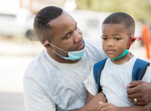 Father consoles anxious kindergartener while they wear masks as he's dropping him off for first day of school,