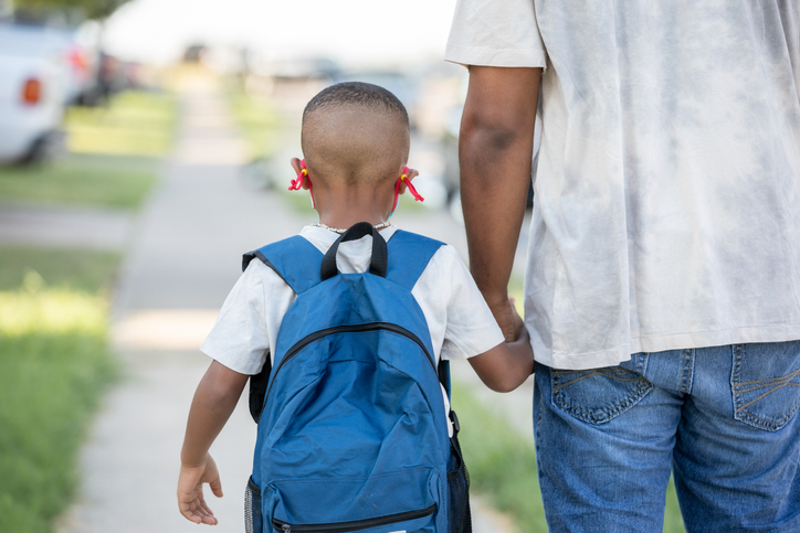 Father holding elementary age sons hand while walking to school