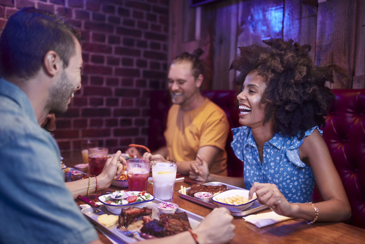Group of multi-ethnic friends laughing and enjoying meal in restaurant
