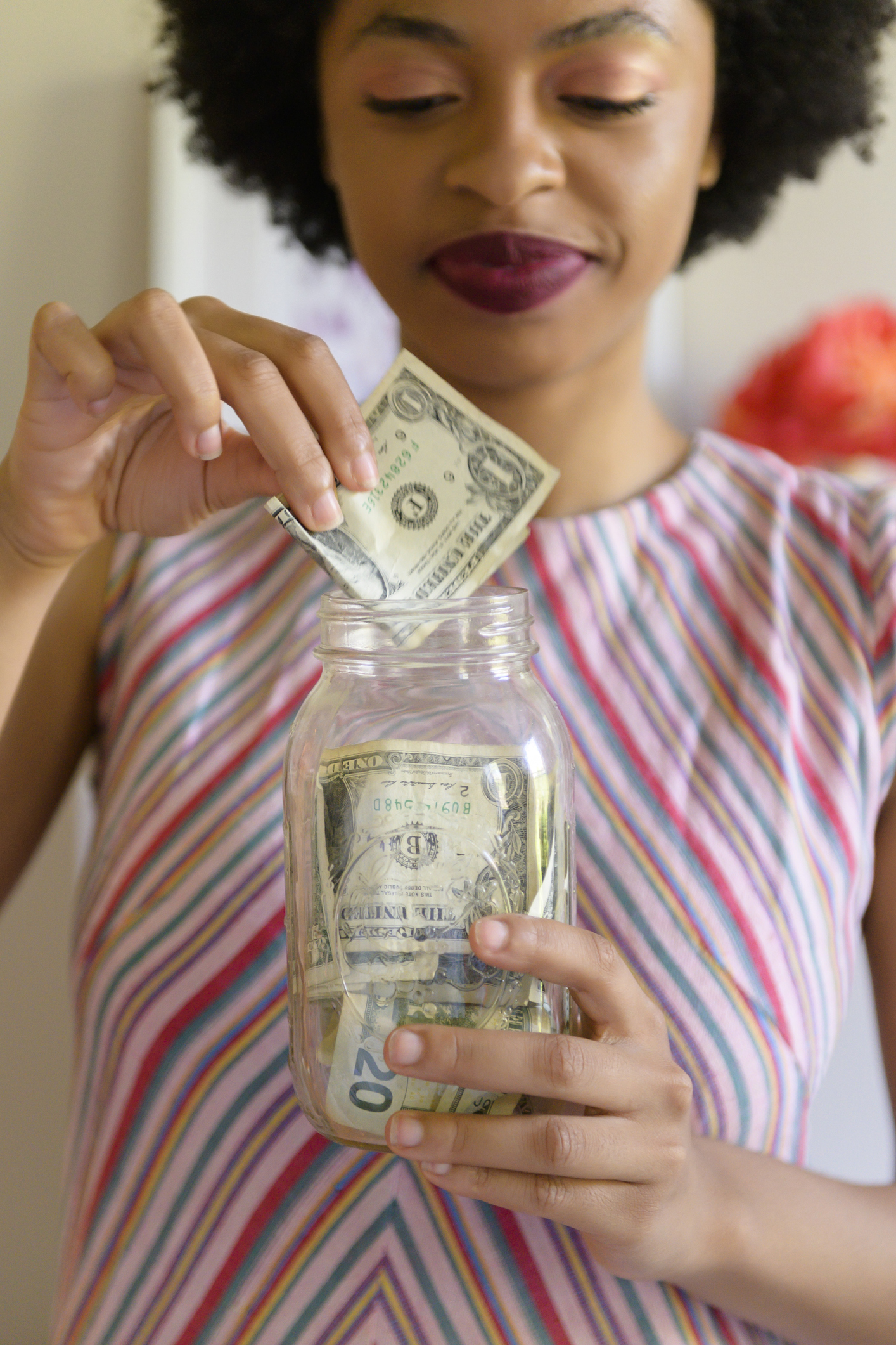 Young woman putting cash into savings jar