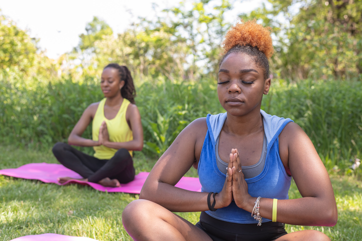 Two African American women in activewear practice yoga together outside