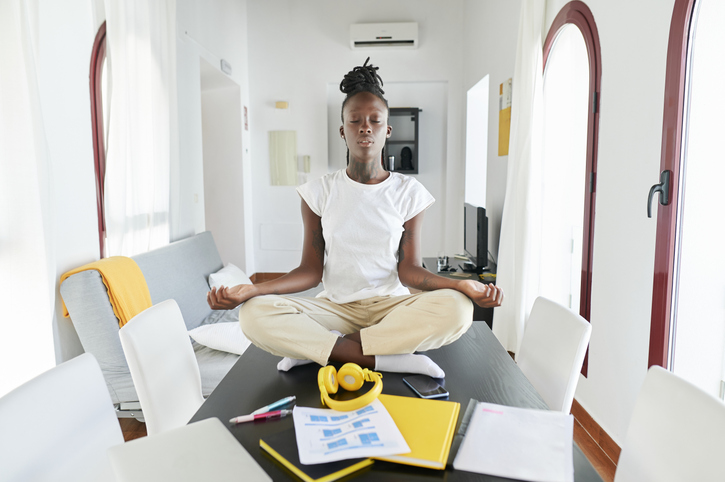 Businesswoman meditating while sitting by laptop and book on desk at home