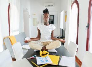 Businesswoman meditating while sitting by laptop and book on desk at home