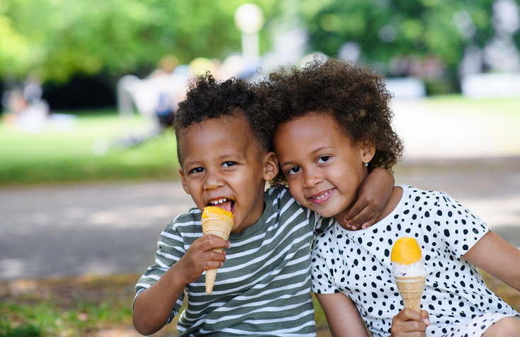 Two small mixed race children in park in city, eating ice cream.