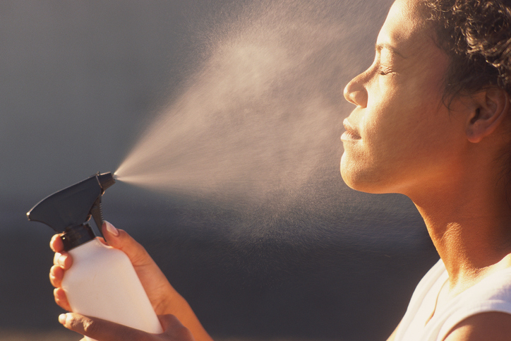 Woman spraying face with water mist