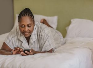 African American woman lying on her bed using a cellphone