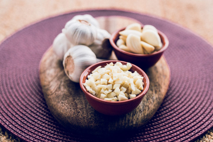 close-up composition of a whole, peeled and chopped garlic on a wooden kitchen board