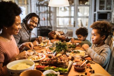 Happy black parents and their kids talking during Thanksgiving dinner at home.