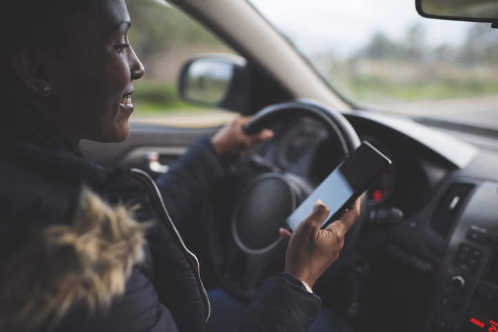 Woman driver scrolling, using smartphone while driving a car.