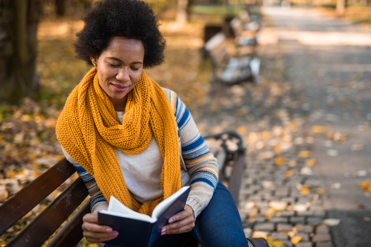 Young African American woman reading a book in the public park.