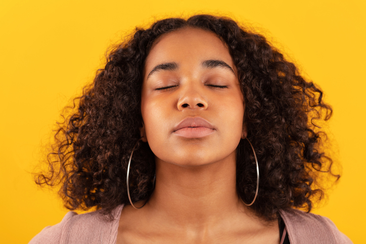 woman with eyes closed meditating against yellow background