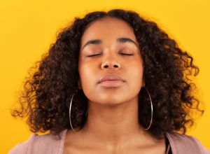 woman with eyes closed meditating against yellow background
