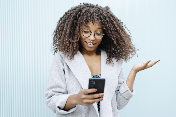 Young woman with African roots and curly hair looking at her smartphone - Stock photo