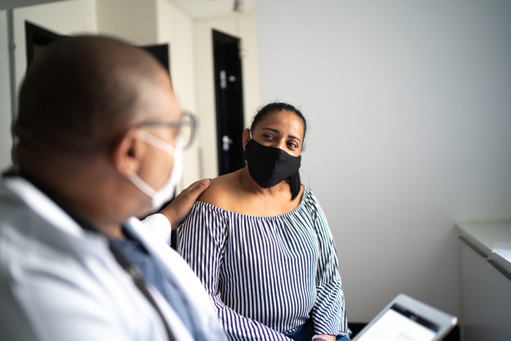 Doctor on a emotional support to a senior patient at home visit - using face mask